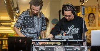 photo of 2 DJs with their heads down over the deck and their headphones on