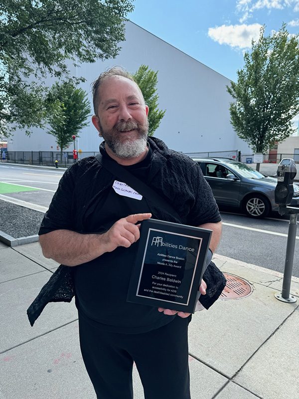 photo of a smiling middle aged man wearing all black and holding a plaque award object.