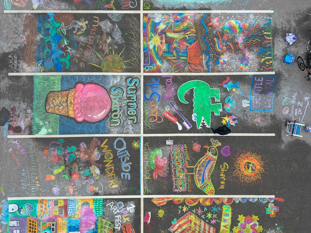 photo of an aerial view of a parking lot with the spaces meant for cars covered in bright chalk drawings