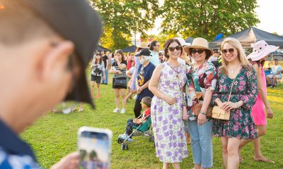 photo of a person holding a phone to take a picture of 3 smiling friends attending an outdoor festival