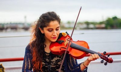 Photograph of a Latina woman deep in the experience of playing her violin, with the Boston Harbor behind her in the distance.