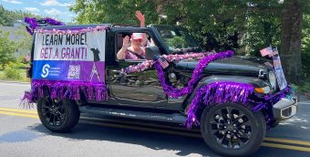 photo of a black Jeep covered in purple shimmery garland and a large banner that reads Learn More, Get a Grant.
