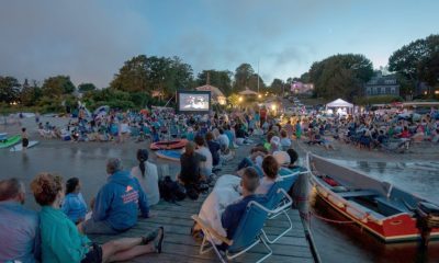 photo of hundreds of people sitting on the beach at dusk watching a film projected on a screen.