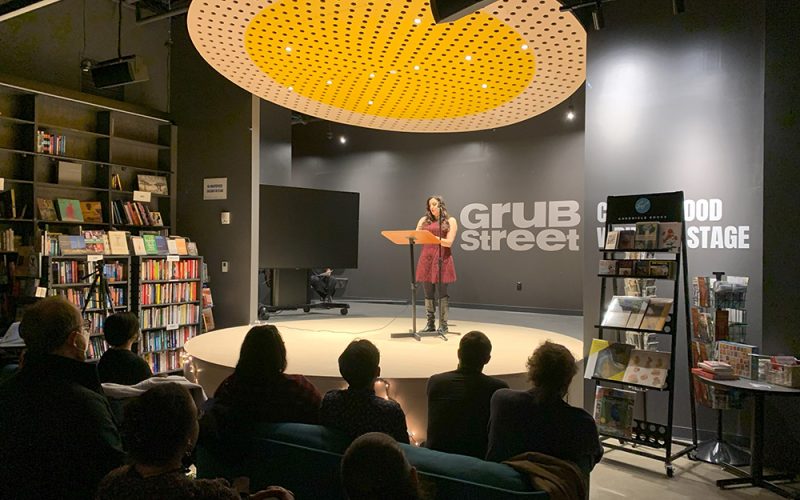 Person on stage at a podium before an audience at Grub Street