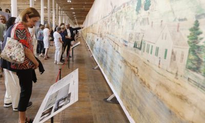 photo of people standing along a wall of a gallery looking at a panoramic painting at tall as the room and longer than the Empire State Building.