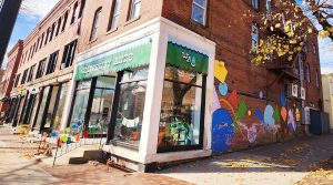 photo of a colorful storefront on the corner of a town's main street. Along the side of the building is a mural of large, brightly colored geometric shapes.