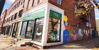 photo of a colorful storefront on the corner of a town's main street. Along the side of the building is a mural of large, brightly colored geometric shapes.