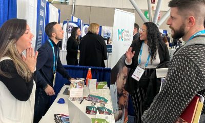 photo of two Mass Cultural staff standing on one side of a long table covered in pamphlets speaking across it to two conference attendees.