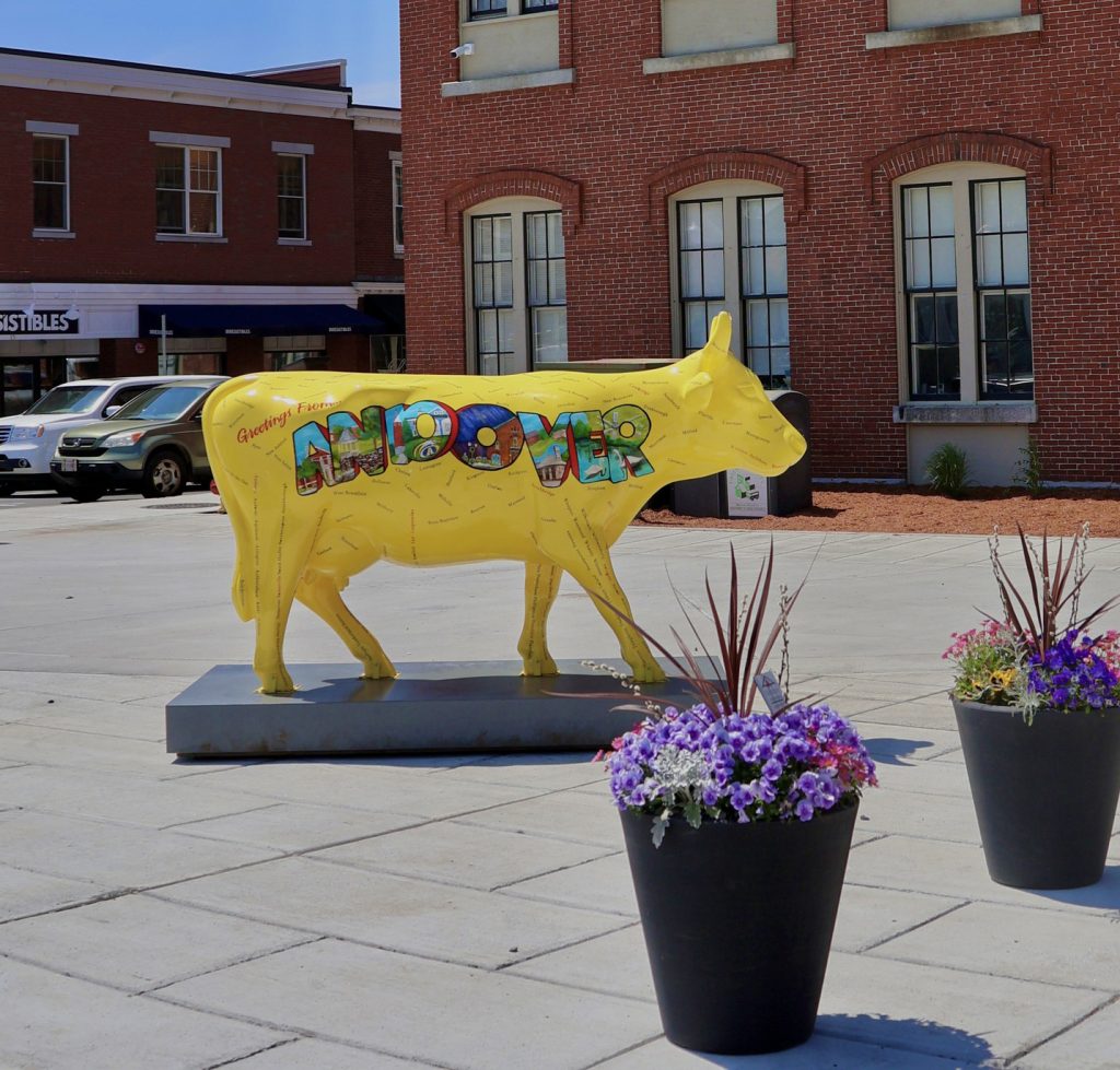 photo of a bright yellow life-size cow sculpture standing in a public square.