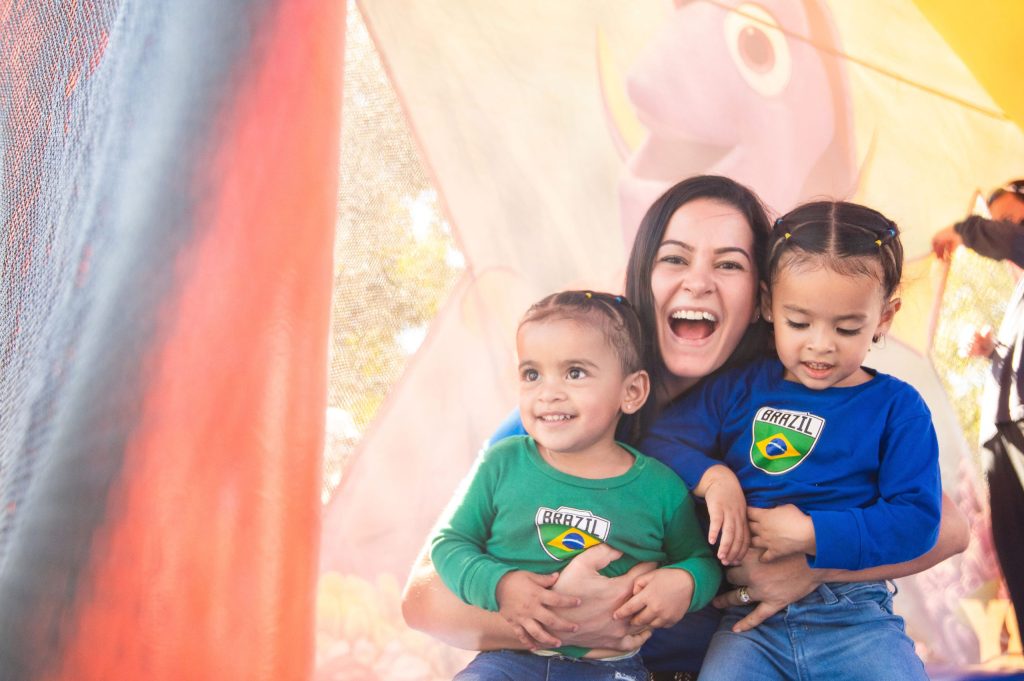 photo of a woman smiling widely and holding two children who are also smiling.