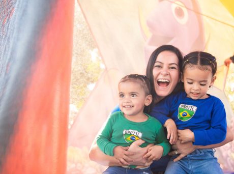 photo of a woman smiling widely and holding two children who are also smiling.