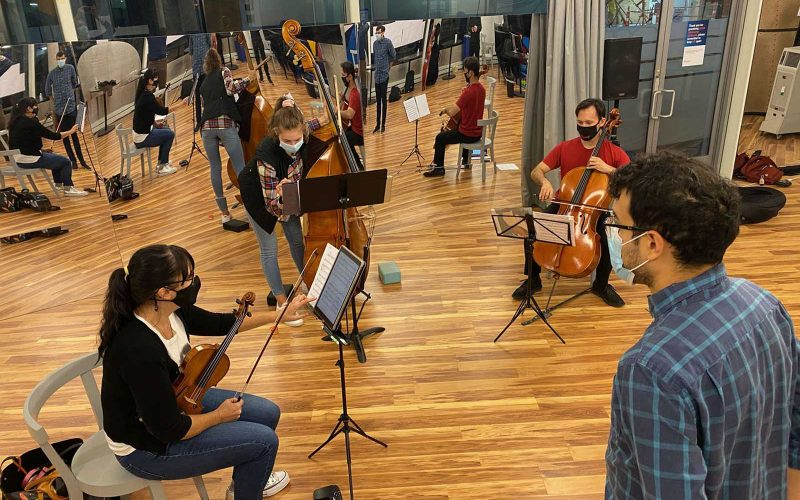 People seated and playing string instruments inside a studio at the Community Art Center in Cambridge
