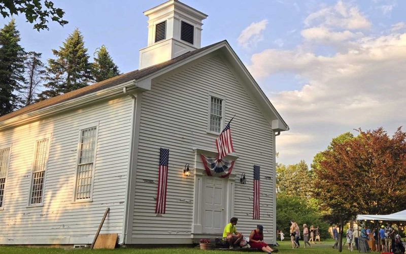 Exterior of a historic meetinghouse with people gathered for an event outdoors