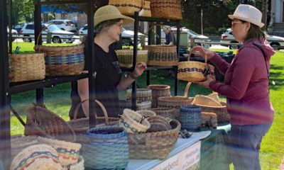 photo of a booth selling baskets at an outdoor festival. There's a woman selling the baskets speaking to a woman standing at the booth.