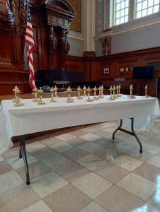 photo of a folding table with a tablecloth and about 20 gold trophy statutes.