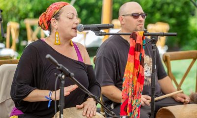 photo of a woman playing a barriles and singing into a microphone with a man standing next to her holding cuá.