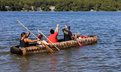 photo of a half dozen adults and children paddling in a canoe made by hand in the tradition of the Herring Pond Wampanoag Tribe.