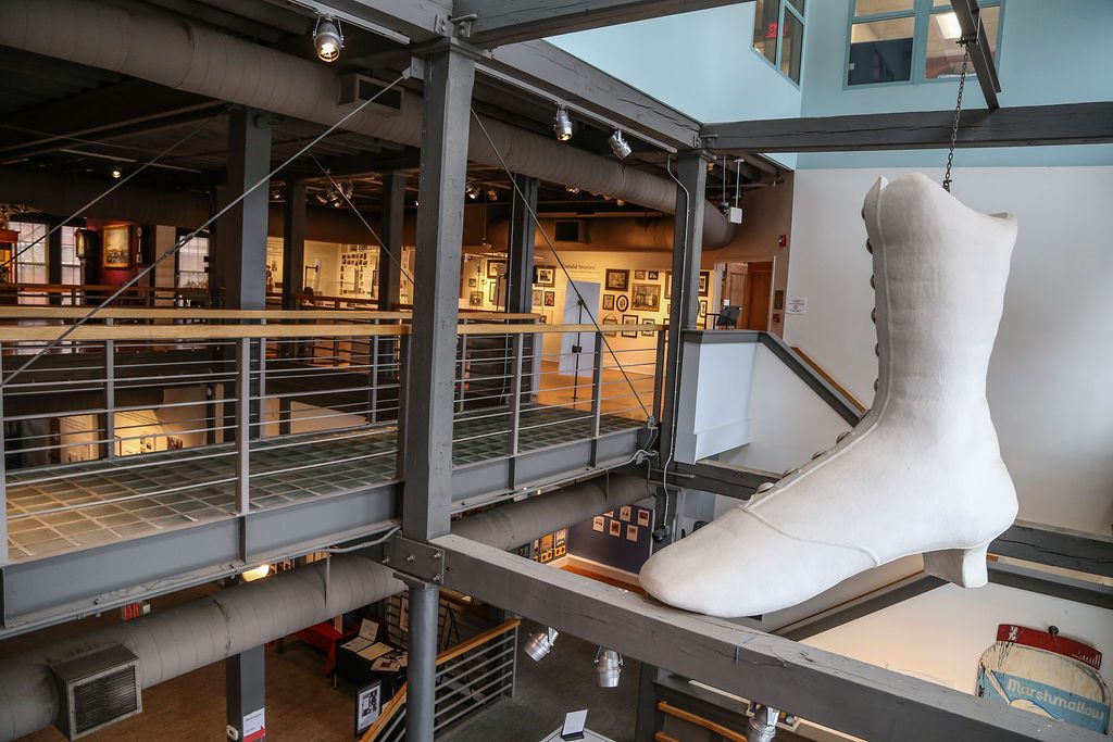 photo of the interior of the Lynn Museum. A large white boot in the style of those worn by women in the late 19th century hangs from the ceiling.
