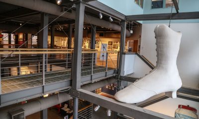 photo of the interior of the Lynn Museum. A large white boot in the style of those worn by women in the late 19th century hangs from the ceiling.