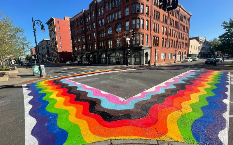 photo of asphalt art of a pride flag painted around a city intersection.