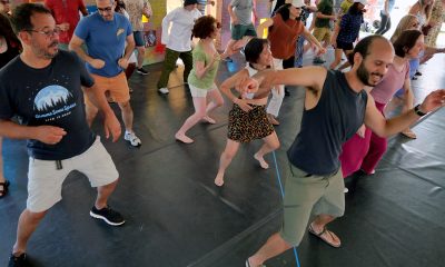 photo of a large group of people of all ages and backgrounds dancing outside under a tent following the instructions of an artist leading them at the front of the class.