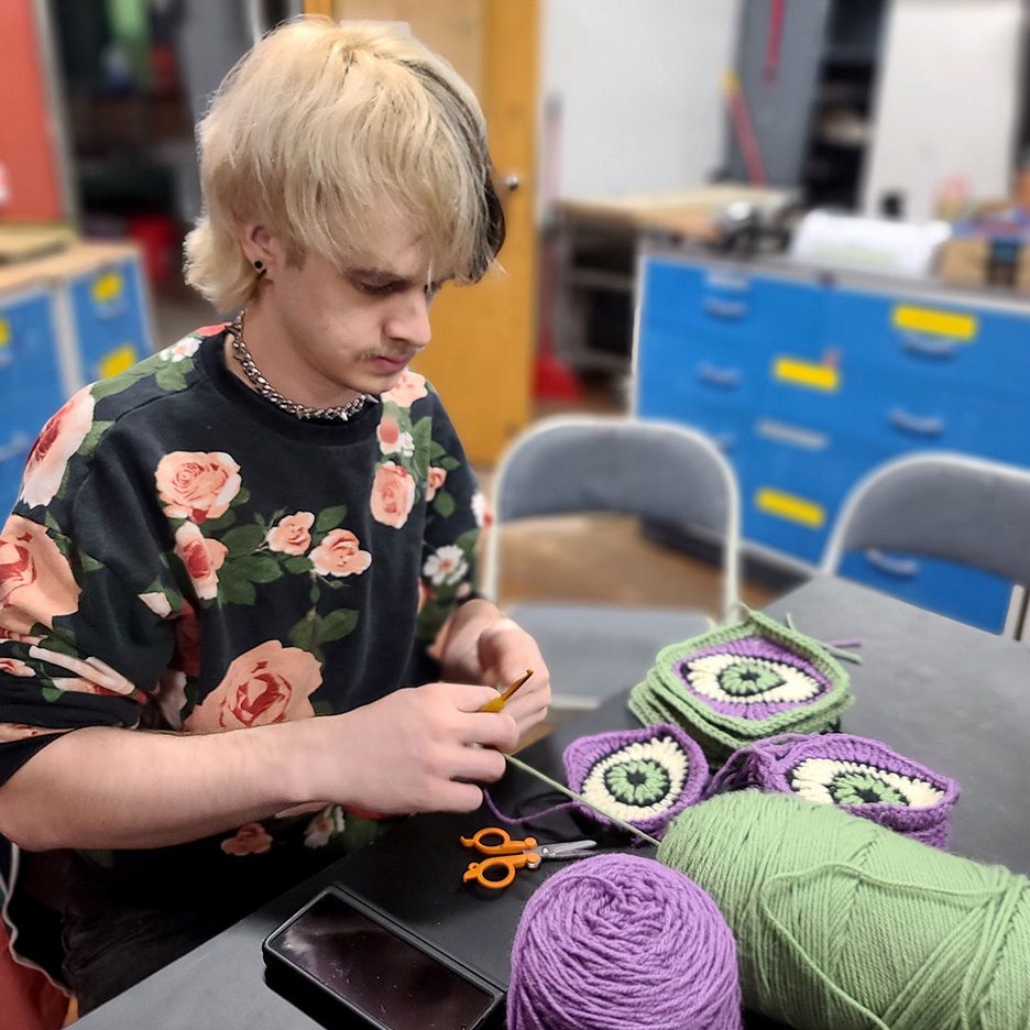 photo of a knitter working on a series of pieces that look like eyes.