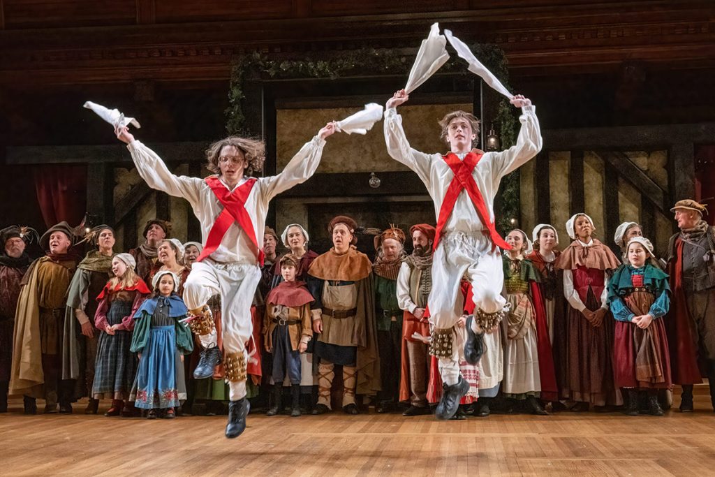 photo from a dance performance where 2 men dressed in late Medieval clothing are jumping into the air, each holding white handkerchiefs in each hand.
