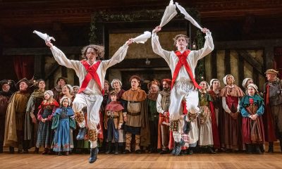 photo from a dance performance where 2 men dressed in late Medieval clothing are jumping into the air, each holding white handkerchiefs in each hand.