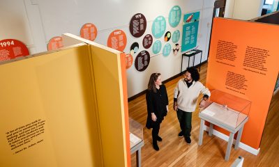 photo of the inside of a gallery. along the back wall is a timeline made of brightly colored circles. in the foreground two people are standing and talking.