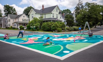 photo of people painting a brightly-colored mural covering a large intersection between 2 main roads.