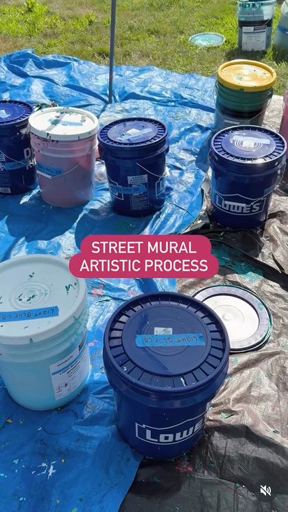 video still showing a blue tarp spread out with various very large buckets of paint placed on it with text Street Mural Artistic process