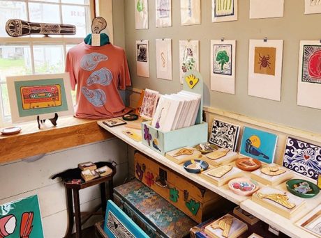 photo of the inside of a shop selling small art works by local artists. many pieces are hanging on the walls and laid out on shelves.