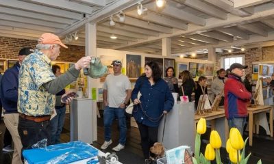 photo of a lively gallery filled with art works and people talking and looking.