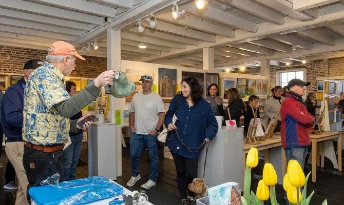 photo of a lively gallery filled with art works and people talking and looking.
