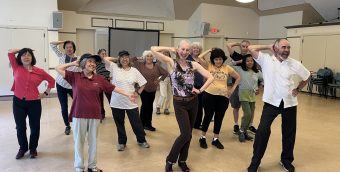 photo of about a dozen older people smiling and dancing in a studio.