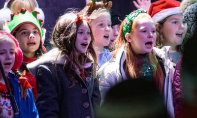 photo of a chorus of children singing, many are wearing festive holiday hats.