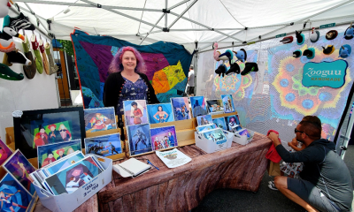 photo of an artist standing in their market stall surrounded by their pieces for sale.