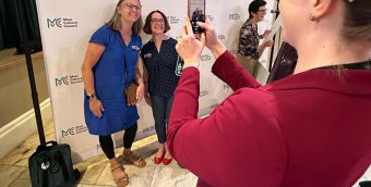 photo of a person taking a photo with their phone of two people smiling at an event.