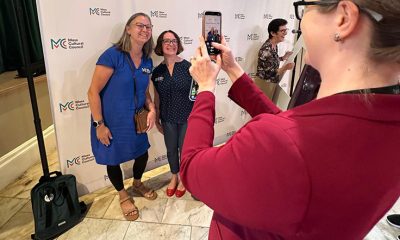 photo of a person taking a photo with their phone of two people smiling at an event.