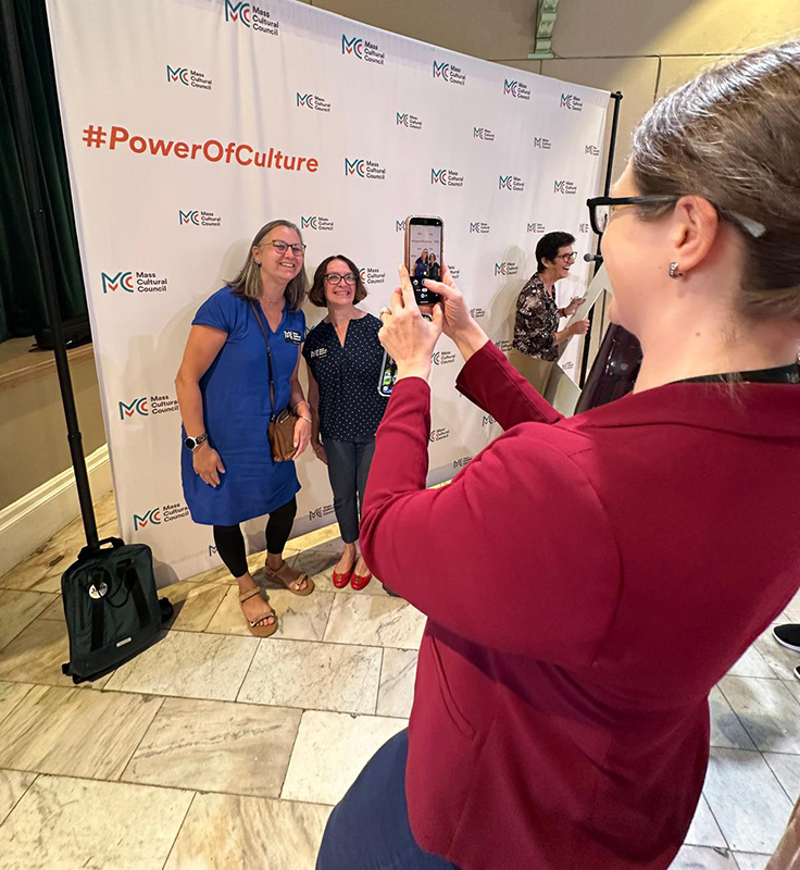photo of a person taking a photo with their phone of two people smiling at an event.