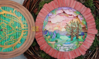 Photo of a vibrantly colored hand-cut paper assemblage that resembles a round door opening onto a peacefully bucolic landscape, sitting within a bird's nest.