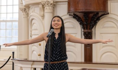 photo of a young person doing a spoken word performance, their arms dramatically outstretched, palms up.