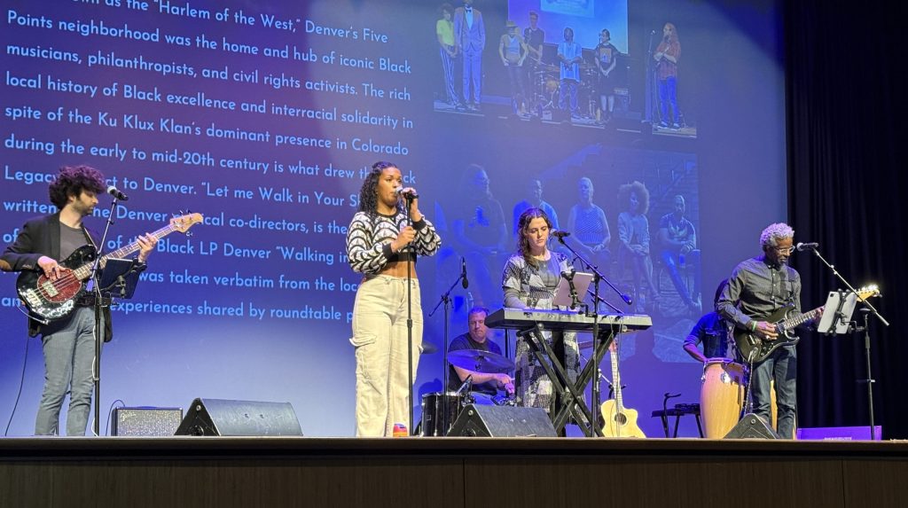 photo of 4 musicians and a vocalist performing on stage. Behind them, a large screen of text and images tell a story of the quote Harlem of the West unquote, Denver's Five Points neighborhood.