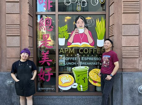 photo of smiling people standing outside a coffee shop with a colorful mural painted on its front window.