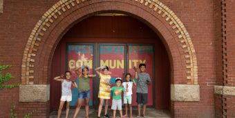a group of young people standing in front of the Cogswell Artspace building, their raised hands covered in paint.