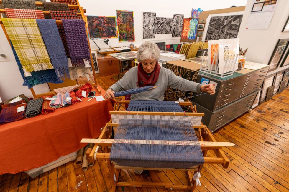 photo of a fiber artist seated at the loom working.