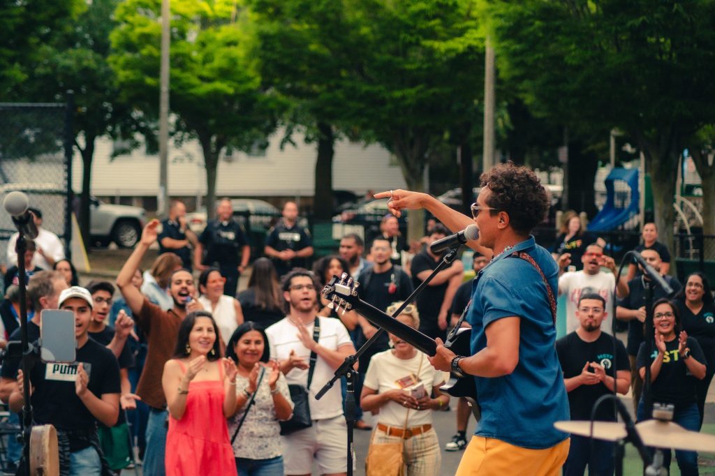photo of a crowd dancing and clapping to a live music performance in a park.