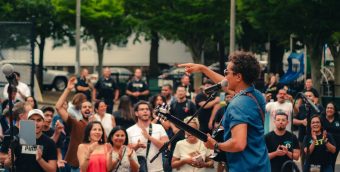 photo of a crowd dancing and clapping to a live music performance in a park.