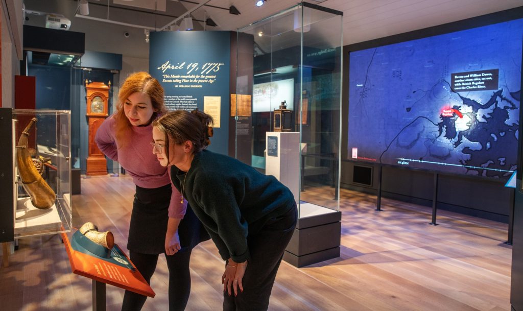 two visitors leaning into a display case in a gallery looking at a couple of pieces of scrimshaw.