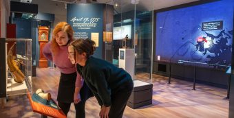 two visitors leaning into a display case in a gallery looking at a couple of pieces of scrimshaw.